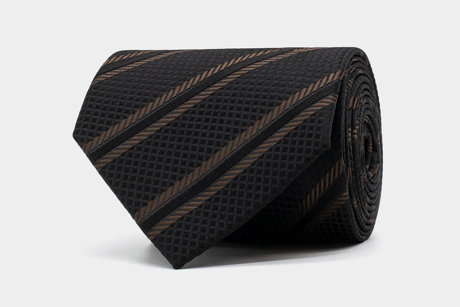 Ornamental Weave Krawatte Schwarz-Braun – festliche Struktur mit dezentem Glanz. Aufgerollte Krawatte aus der Kollektion Ornamental Weave in Schwarz-Braun mit diagonalen Streifen und feiner Struktur auf hellem Hintergrund.