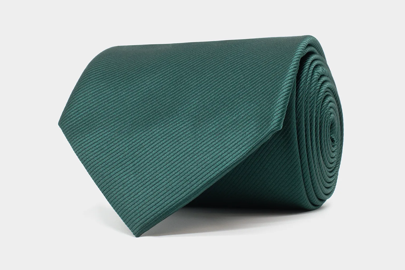 Noble Lines Krawatte in Dunkelgrün – elegante Struktur und tiefe Farbsättigung. Aufgerollte dunkelgrüne Krawatte aus der Kollektion Noble Lines, gefertigt aus fein gerippter Seide auf hellem Hintergrund.