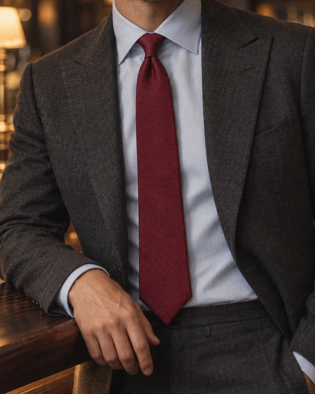 Nahaufnahme einer weinroten Krawatte Heritage Silk zum anthrazitfarbenen Flanellanzug und hellblauen Hemd an einer Bar Nahaufnahme einer weinroten Krawatte Heritage Silk zum anthrazitfarbenen Flanellanzug und hellblauen Hemd an einer Bar