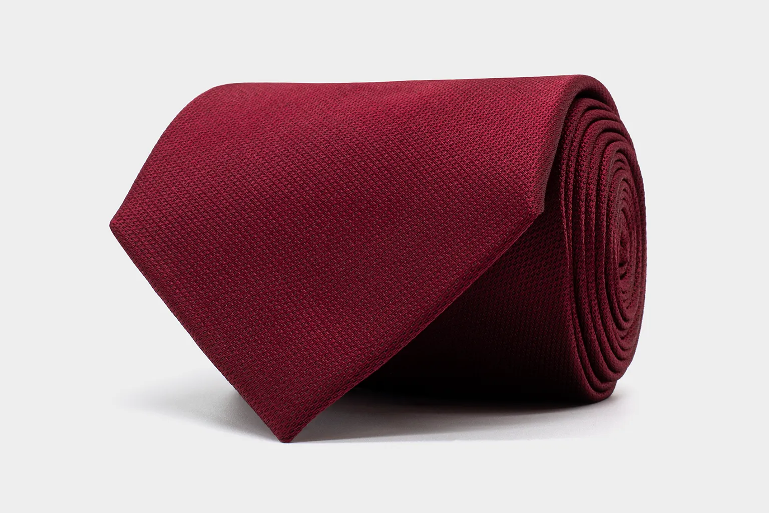 Heritage Silk Krawatte in Bordeaux – charaktervolle Tiefe und klassische Eleganz. Aufgerollte bordeauxrote Krawatte aus reiner Seide aus der Kollektion Heritage Silk, mit feiner Webstruktur auf hellem Hintergrund.